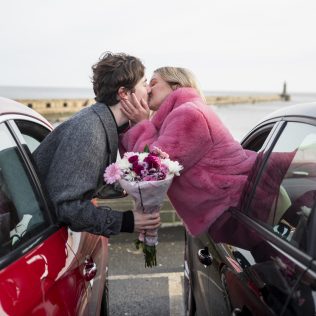 Couple leaning out of two cars in the North East of England during the Covid pandemic. The man is giving his girlfriend a bunch of flowers.